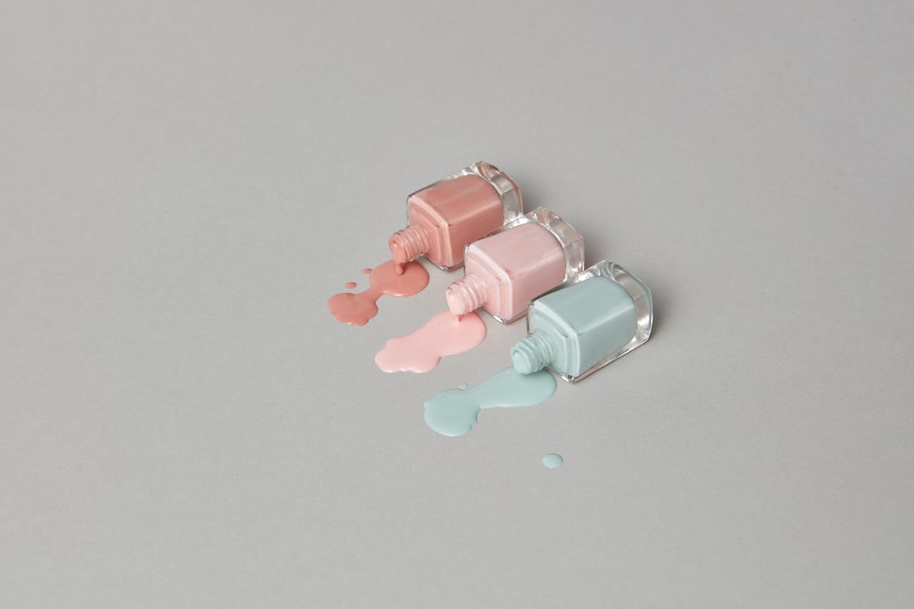 Three pastel nail polish bottles spilling on a minimalist grey background, creating a soothing aesthetic.