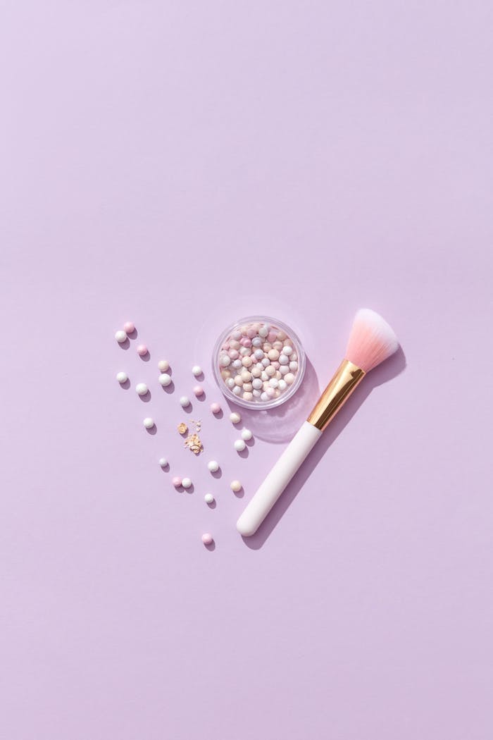 about-img-02 Flat lay of a makeup brush and pearlescent beads on a lavender background, highlighting beauty essentials.