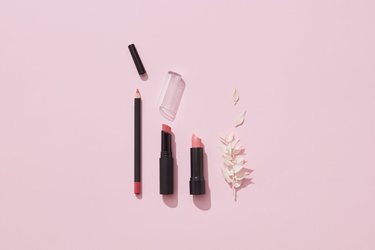 hero-gallery-02 Flat lay of lipsticks and lip pencil with leaves on pink background.