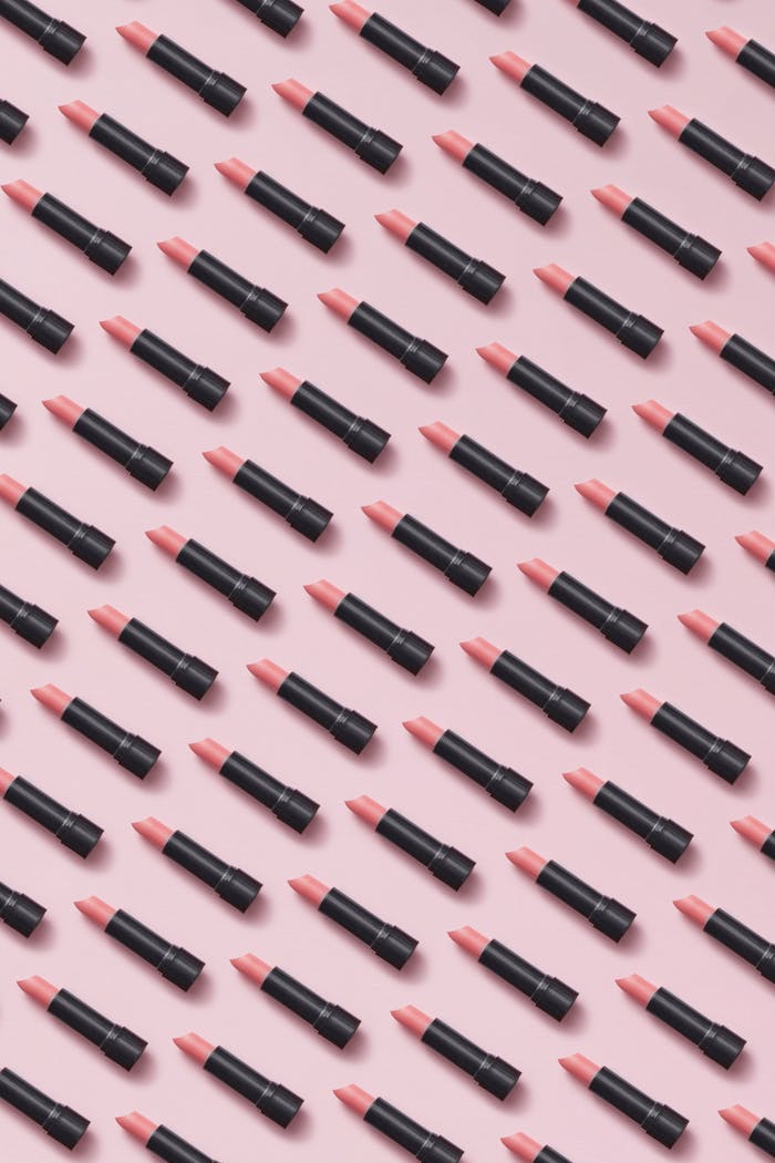 Aesthetic arrangement of pink lipsticks creating a modern pattern on a pastel surface.